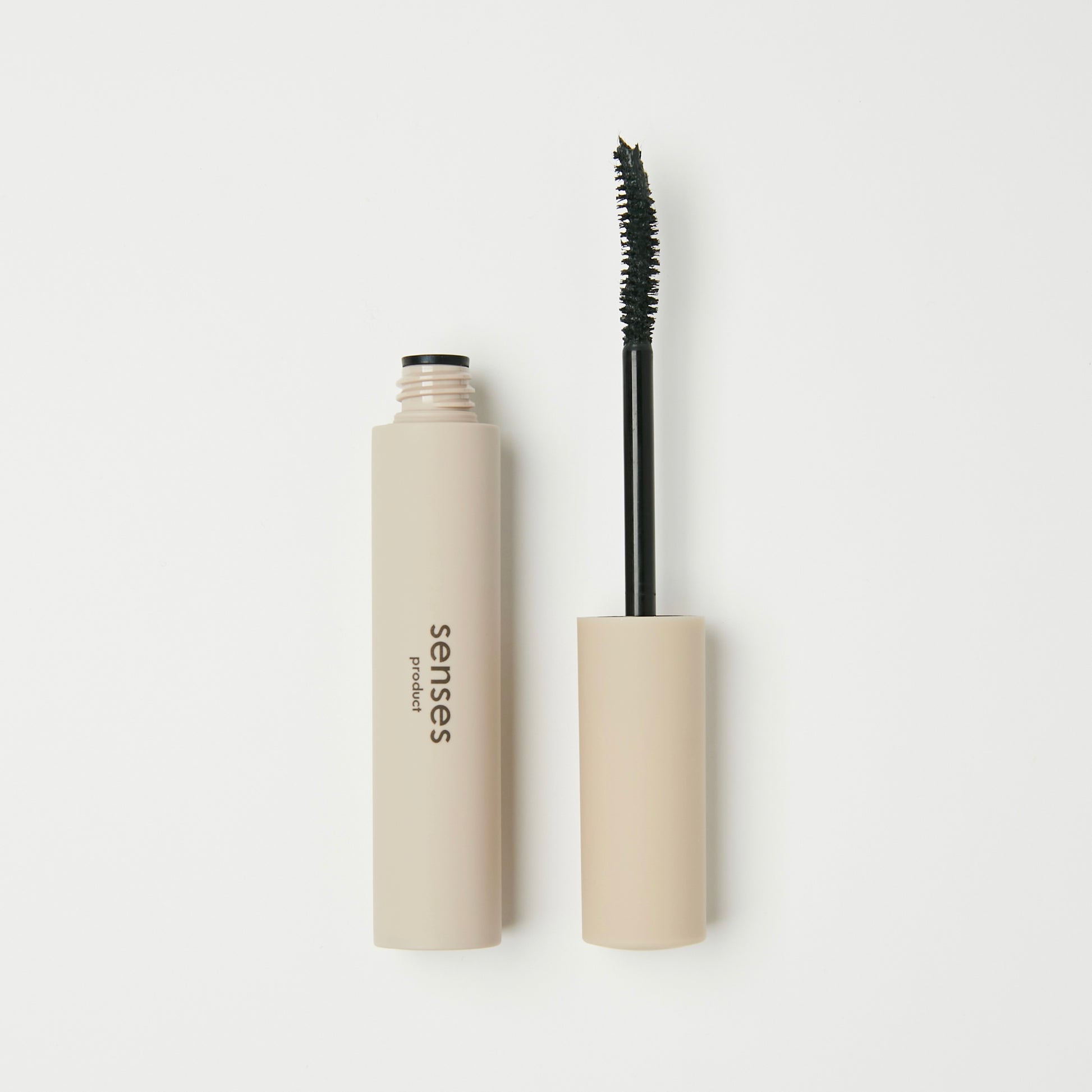 An open beige mascara tube with the wand beside it on a white background.