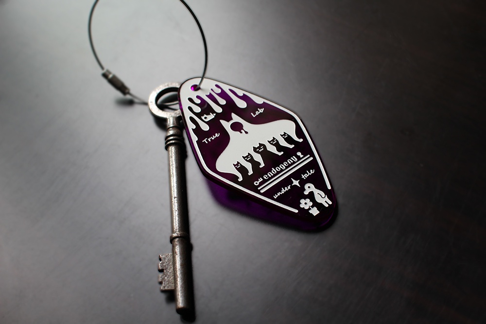 Photo of a purple motel-style acrylic keychain attached to a metal key on a wire loop lying on a dark surface.