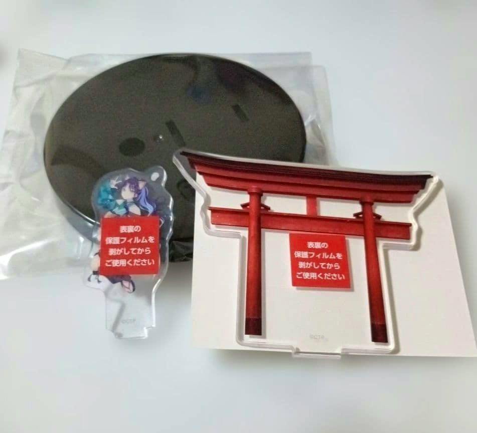 Photo of the acrylic stand and cup holder components: a round black base, a torii-shaped acrylic piece, and a small character acrylic piece with protective film.