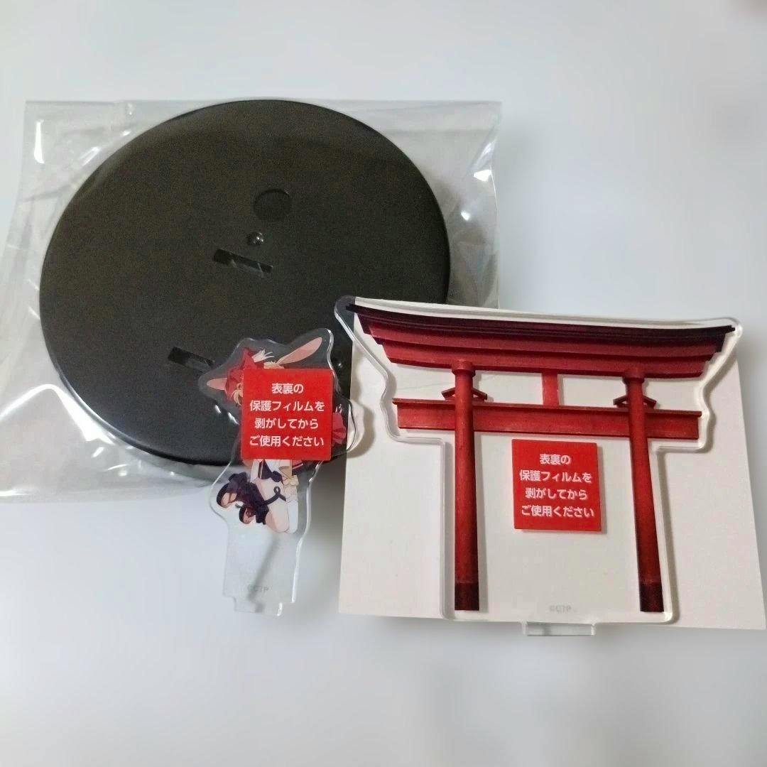 Photo of the acrylic drink cup holder set showing a black round base in plastic, a torii-gate shaped acrylic insert, and a small character acrylic piece with protective-film stickers.