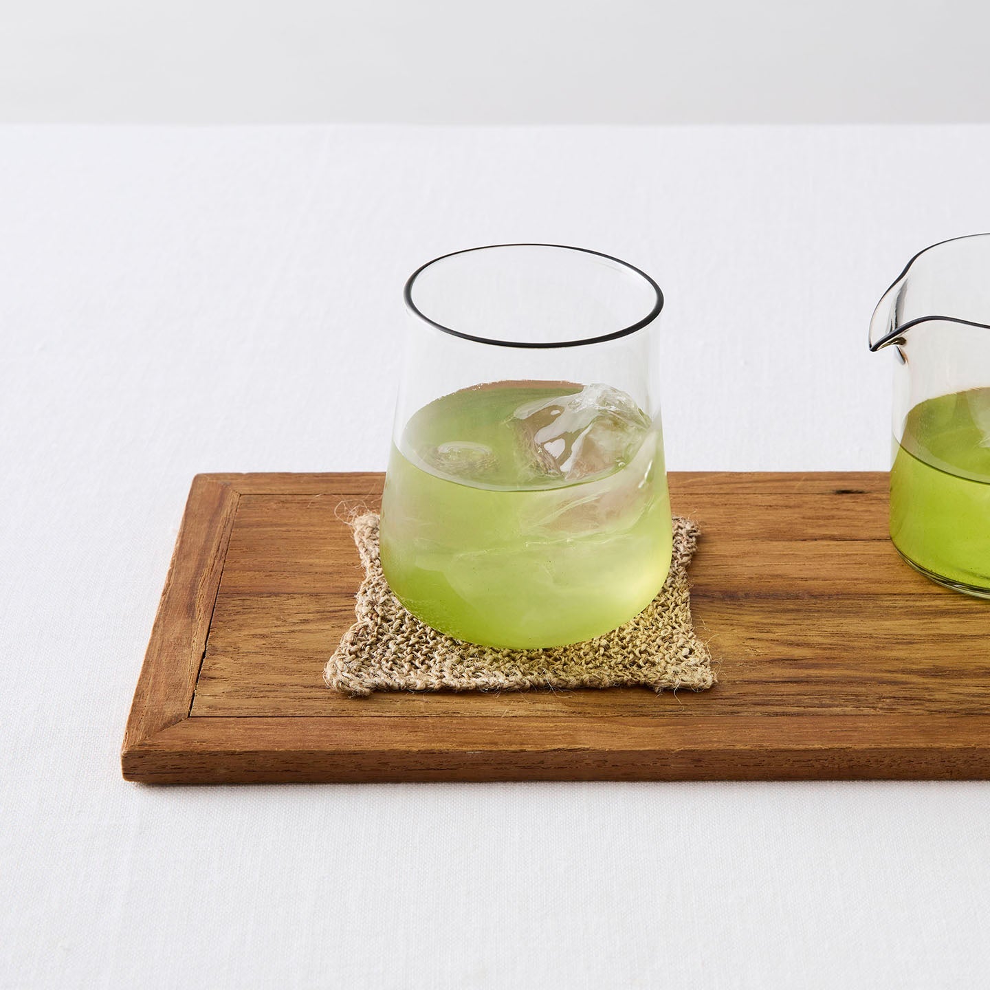 A knitted coaster (coaster, linen) placed under a glass with a green drink on a wooden tray.