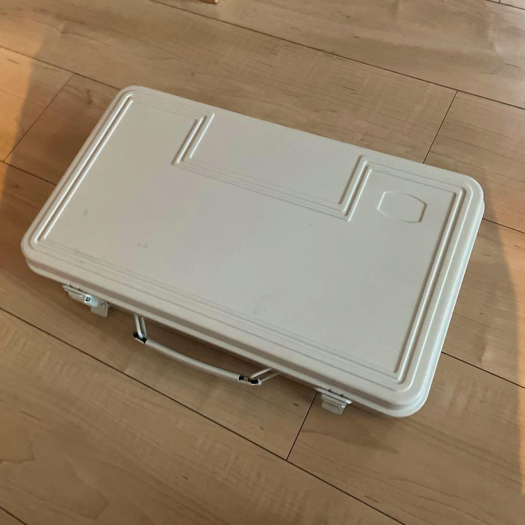 Closed Muji steel toolbox on a wooden floor, shown from above with handle and latches visible.