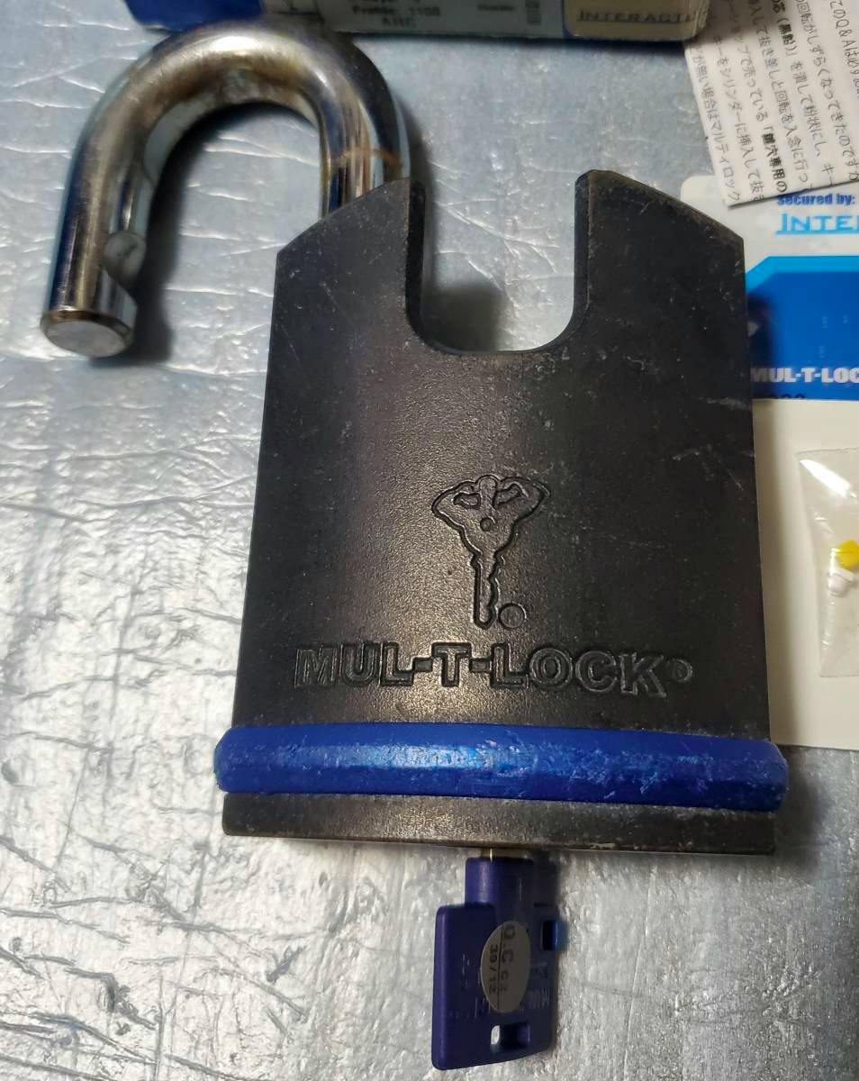 MUL-T-LOCK padlock body with the shackle open and a blue key inserted, showing the embossed MUL-T-LOCK logo.