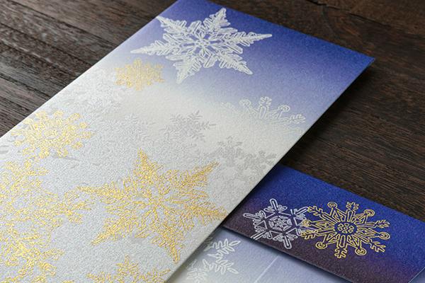 A multipurpose envelope with a blue-to-white gradient and gold and silver snowflake pattern on a wooden surface.
