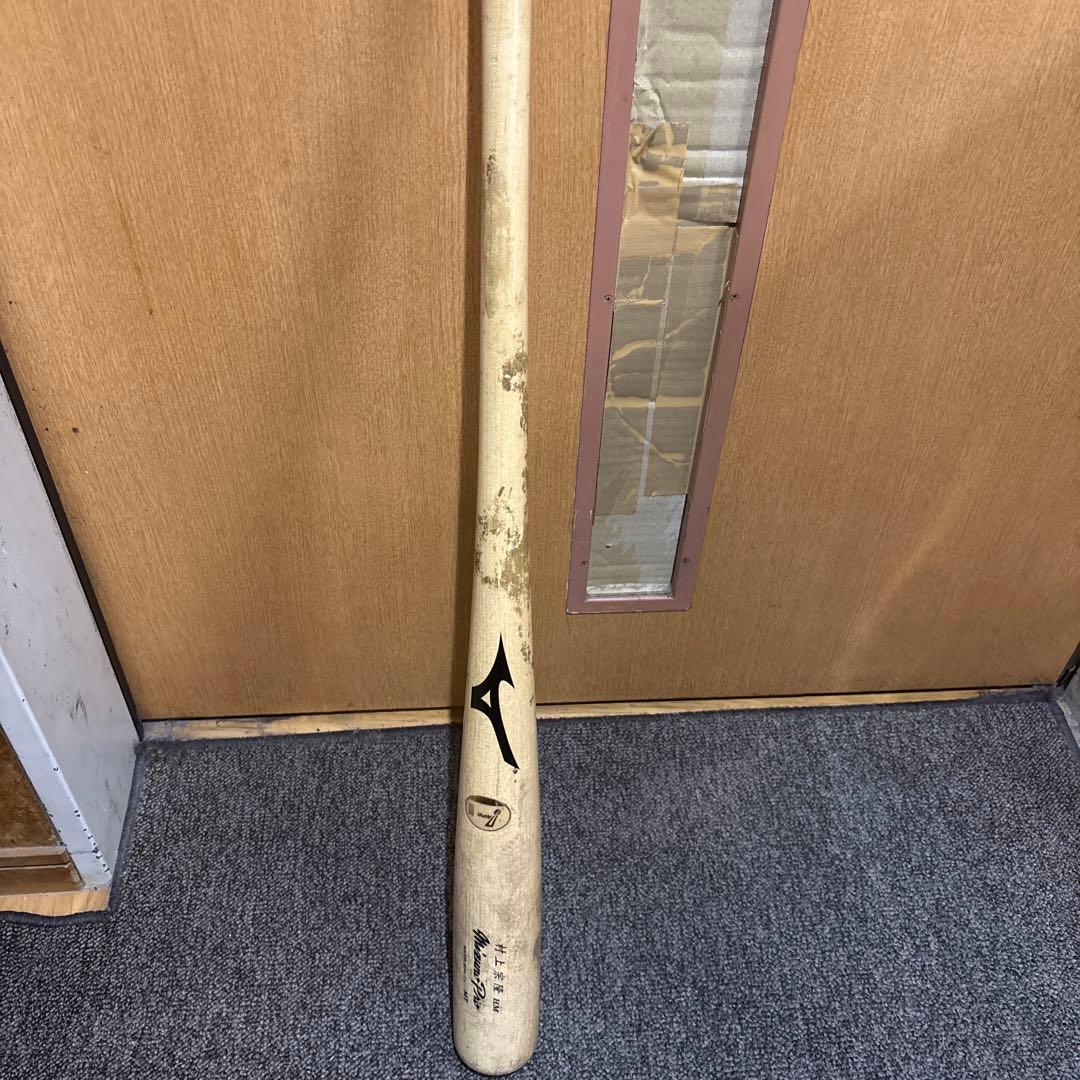 Official NPB wooden baseball bat with visible scuff marks leaning against a wooden door on a carpeted floor.