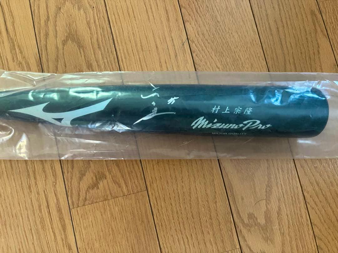 Barrel of a MizunoPro baseball bat showing a white Mizuno logo, printed Japanese text, and a signature inside plastic on a wooden floor.