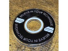 A circular lever disk for a joystick with the text "BELIEVE IN YOUR TECHNIQUE" placed on a wooden surface.