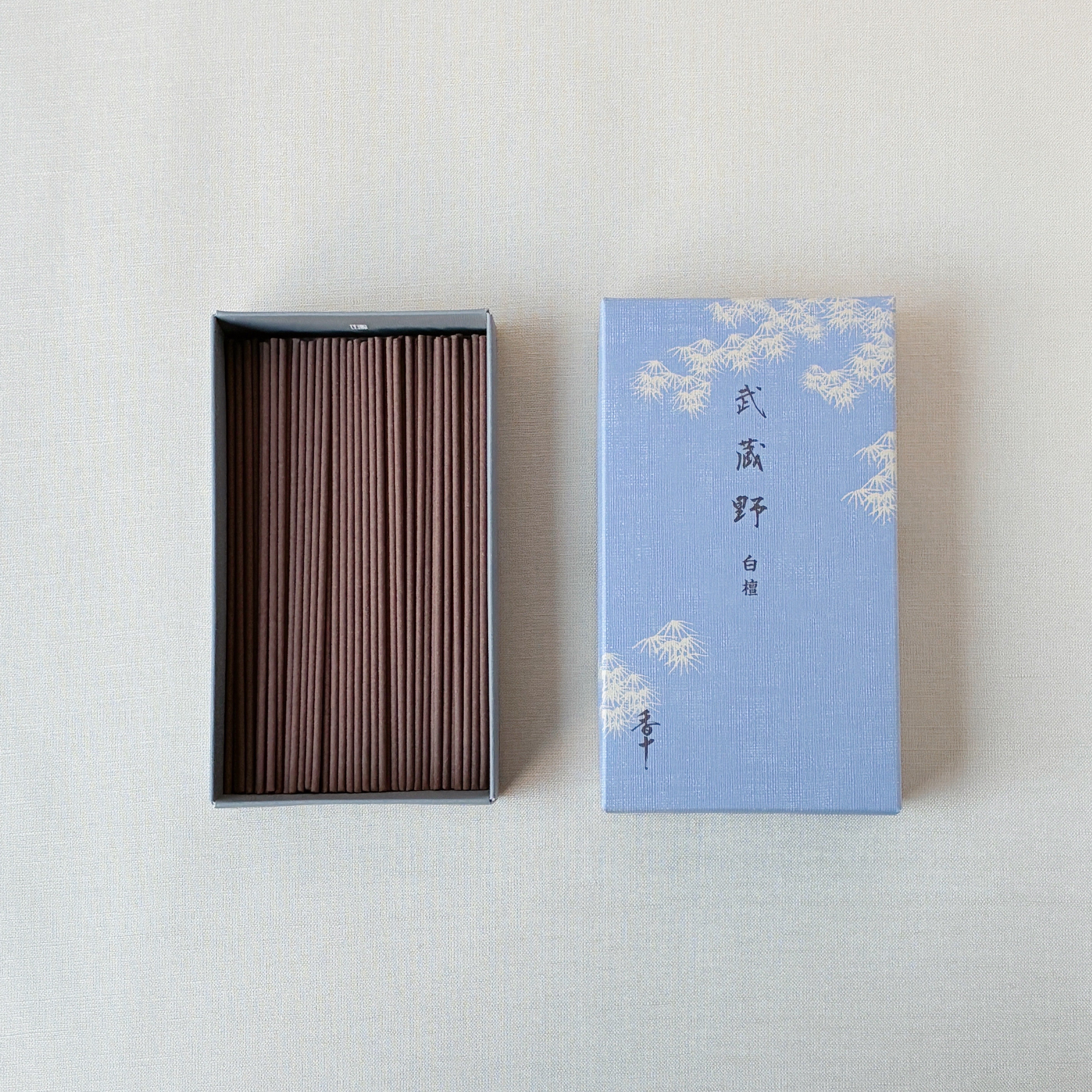 An open box of brown incense sticks displayed next to a blue patterned box labeled with Japanese text.