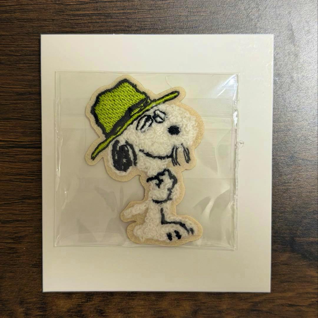Paper sticker of a white dog-like character wearing a green hat, sealed in plastic and mounted on a white card on a wood surface.