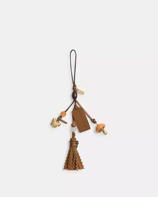 Leather mushroom-themed bag charm with tassel, beads, and a hanging strap on a white background.