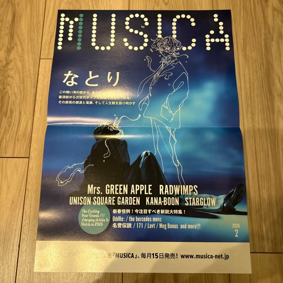 Photograph of the MUSICA 2026年2月号 なとり cover poster laid flat on a wooden floor, showing the blue artwork and text.