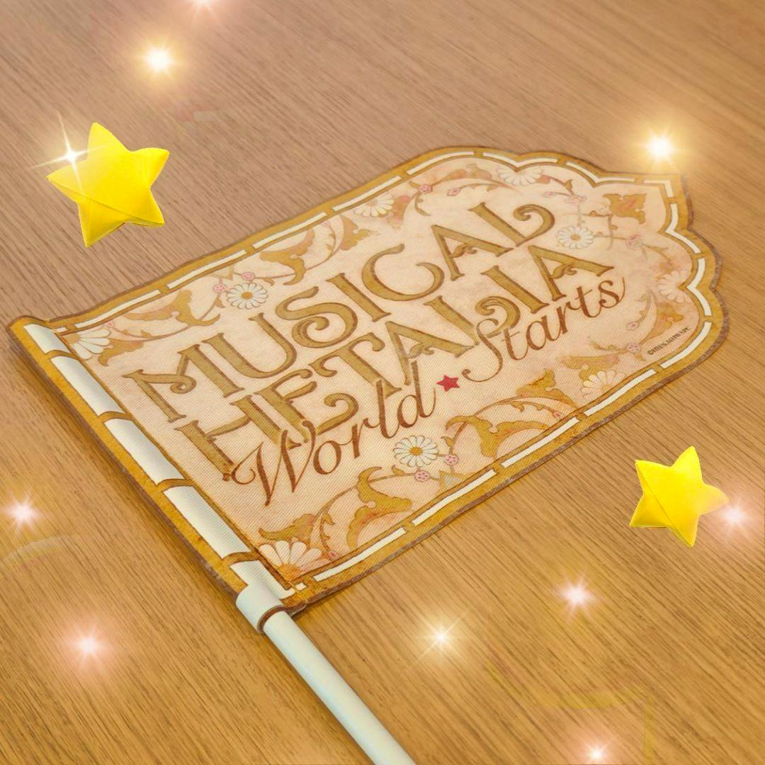 A Musical Hetalia "World Starts" flag laid flat on a wooden surface showing the printed design and attached white pole.
