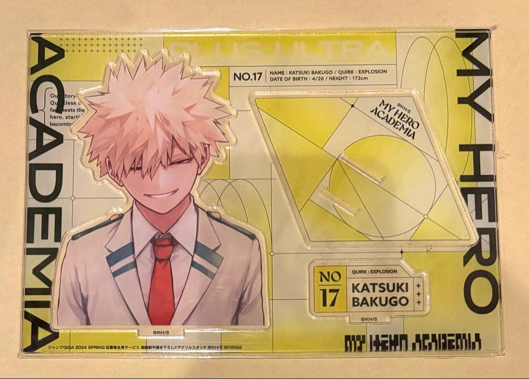Packaged acrylic stand of Katsuki Bakugo showing the character artwork and detachable base pieces on a yellow My Hero Academia backing.