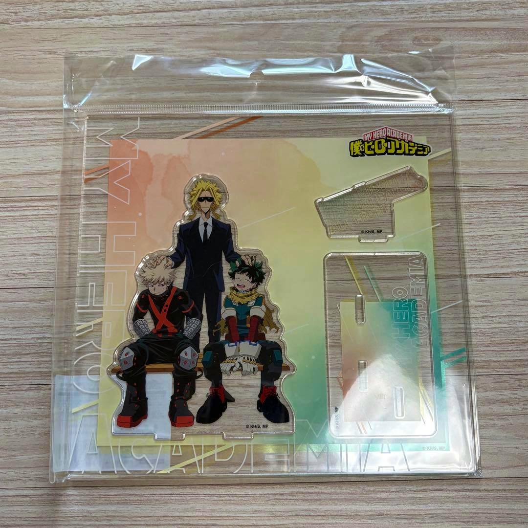 Packaged front-view acrylic stand showing Deku (緑谷出久) and Bakugo (爆豪勝己) seated with a taller character and two separate base pieces visible.