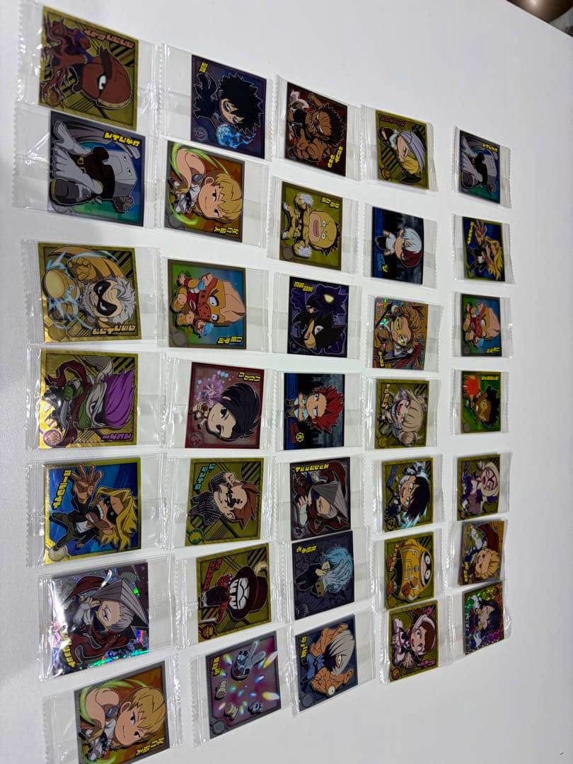 Photo of multiple My Hero Academia wafer-style stickers in individual clear packets arranged on a white surface.