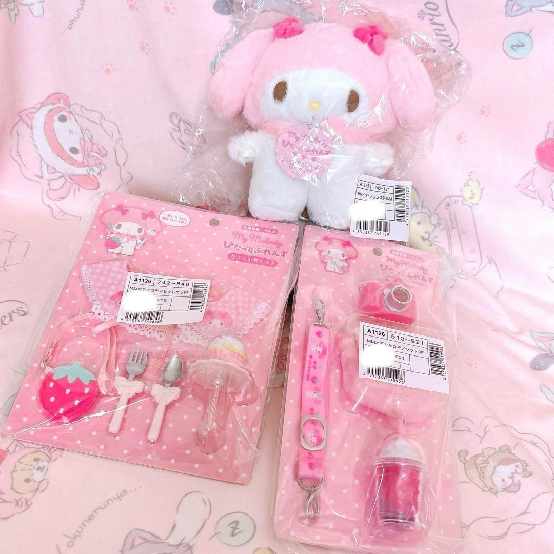 A My Melody M plush doll in plastic wrap accompanied by three pink packaged café-themed small accessory sets displayed on a pink background.