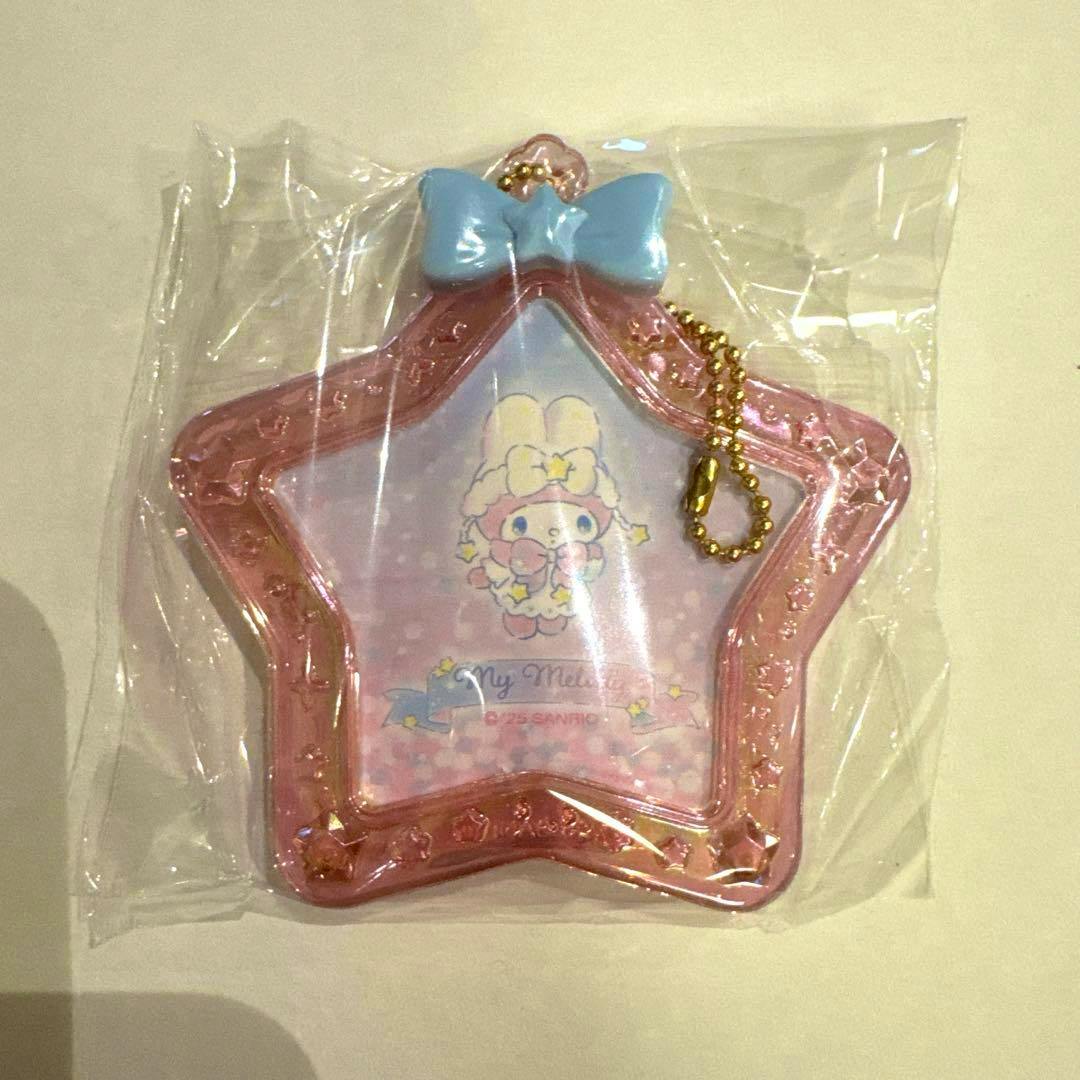 Front view of a star-shaped pink My Melody mini plastic photo frame with a blue bow and gold ball chain, shown in its plastic packaging.