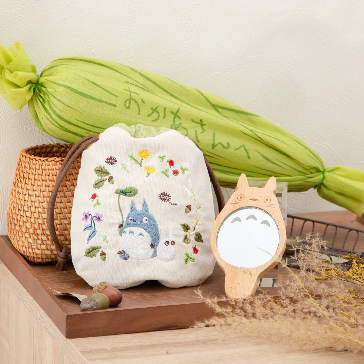 Totoro-shaped compact mirror with wooden finish displayed on a tabletop beside an embroidered drawstring pouch and decorative props.