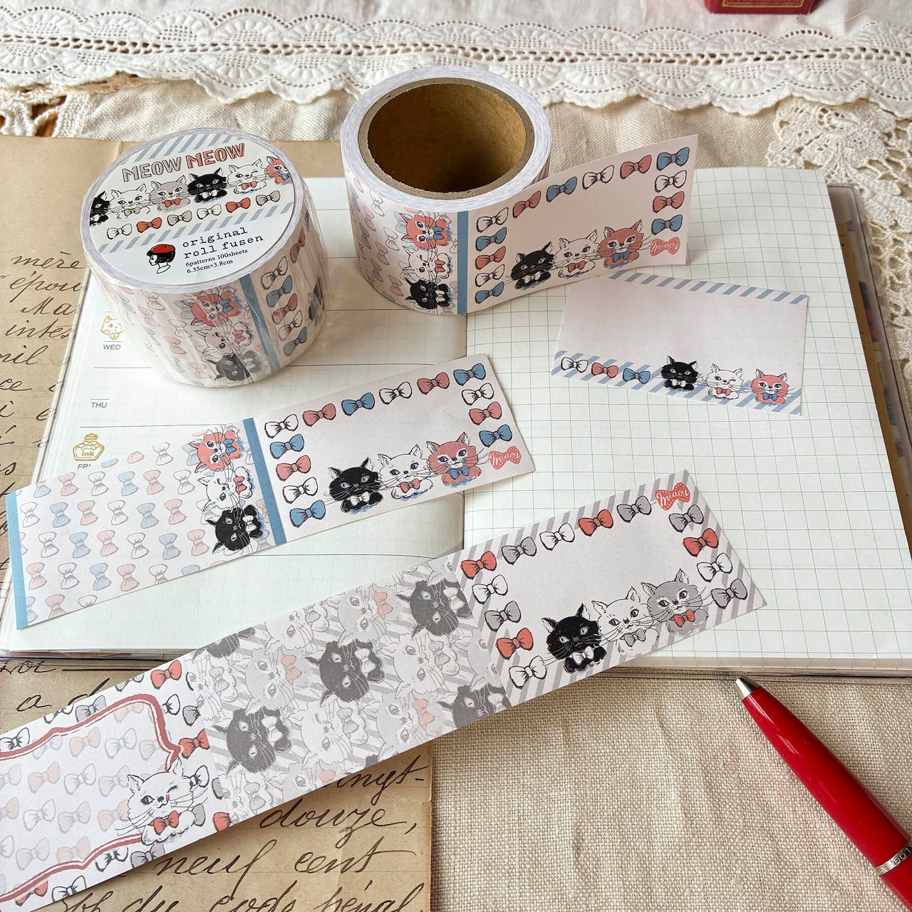 A roll of cat-patterned adhesive memo tape (roll sticky notes) and several unrolled strips showing cat faces and bow designs laid on an open notebook.