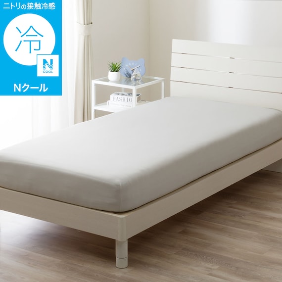 Off-white Nクール fitted sheet covering a mattress on a bed frame in a bright room.