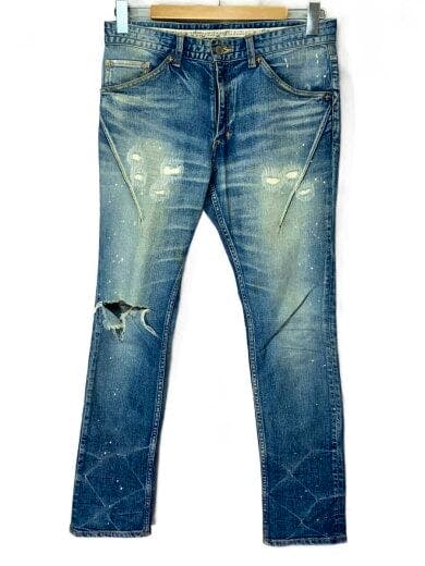 Front view of men's cotton woven blue jeans with distressing and paint-splatter details, hung on a wooden hanger against a white background.