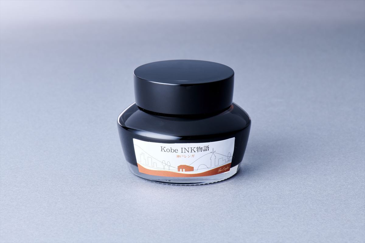 A bottle of Nagasawa Kobe INK Monogatari #39 Kobe Renga (brown-red) fountain pen ink on a gray surface.
