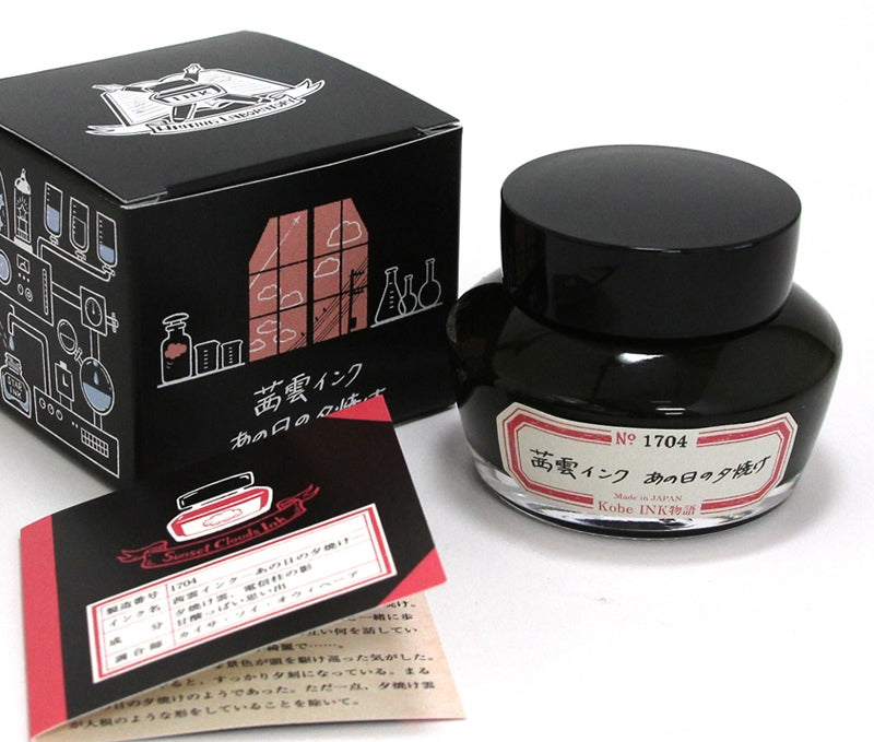 Glass bottle of Nagasawa Kobe fountain pen ink with label beside its black illustrated box and a folded leaflet.