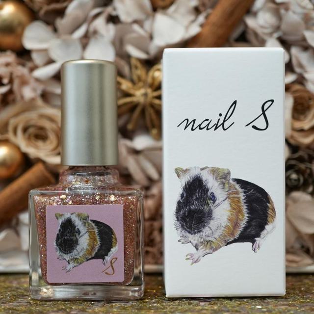 A glass nail polish bottle with pink-gold glitter next to its white product box showing a guinea pig illustration on a decorative background.