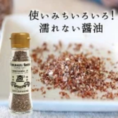 A bottle of powdered soy seasoning beside a plate of scattered seasoning granules with Japanese text in the background.