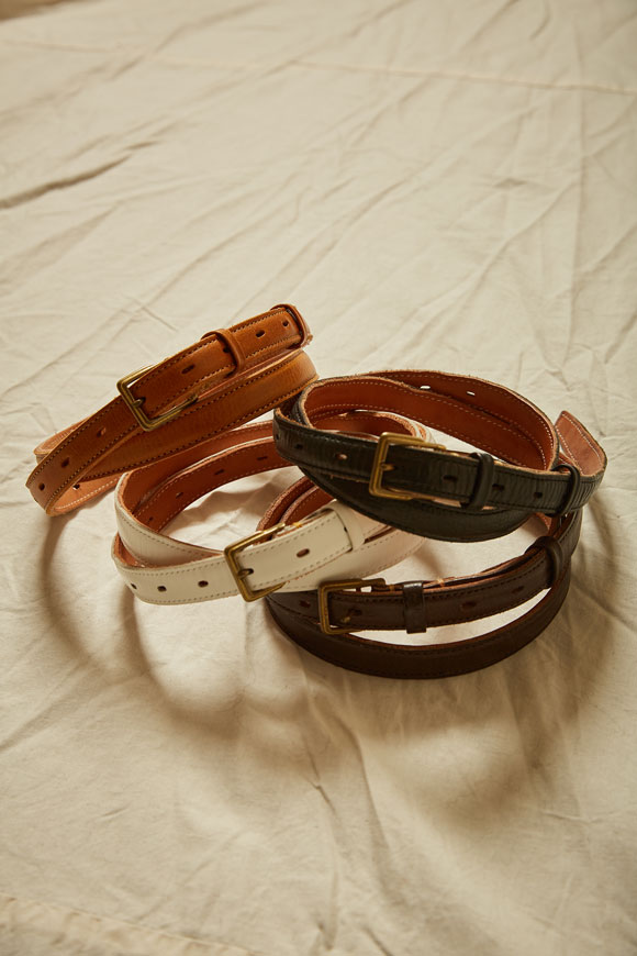 Several narrow cow leather belts in different colors arranged on a cloth background.