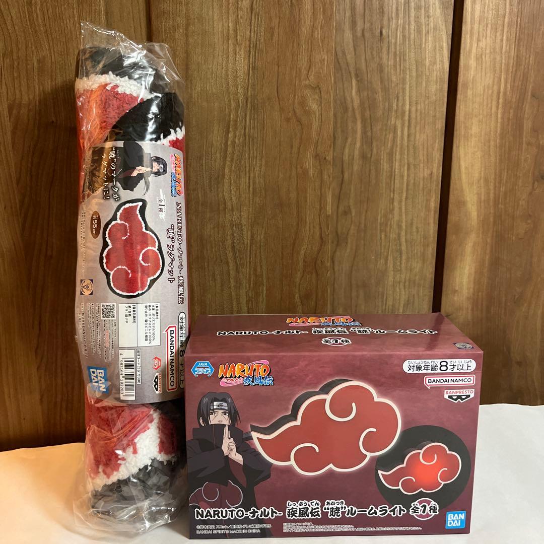 A rolled Akatsuki rug mat in plastic wrap standing beside a boxed Naruto Akatsuki room light on a table against a wood background.