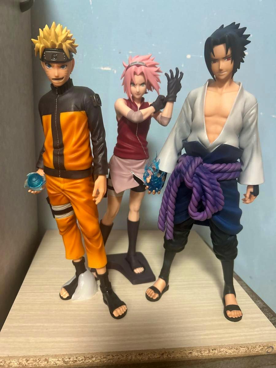 Three Naruto Grandista plastic figures (Naruto, Sakura, Sasuke) standing together on a flat surface against a light blue background.