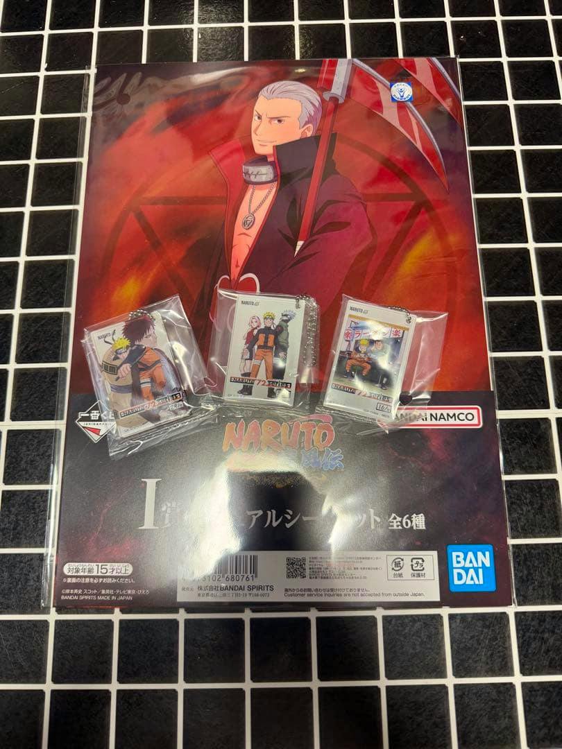 Photo of a Naruto visual sheet poster with three packaged acrylic keychain charms displayed on a black-and-white tiled surface.