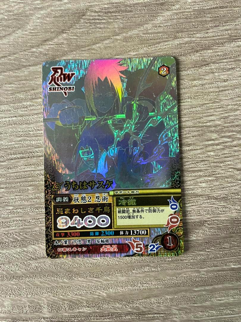 Holographic NARUTO うちはサスケ trading card photographed on a textured surface, showing character artwork and Japanese text.