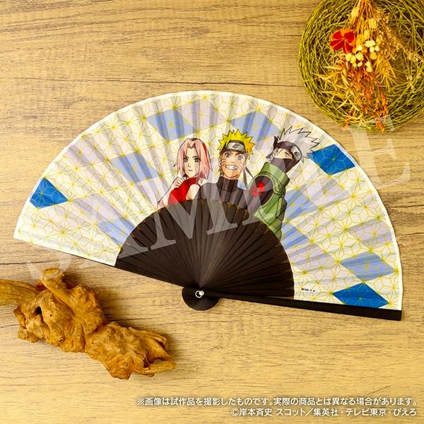 Open paper folding fan featuring Naruto, Sakura, and Kakashi printed on the fan leaf, laid on a wooden surface.