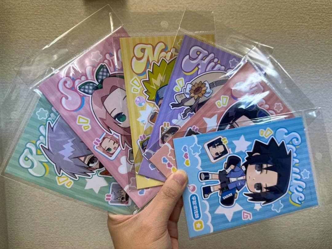 A hand holding six sealed chibi-style Naruto character postcards fanned out in plastic sleeves.