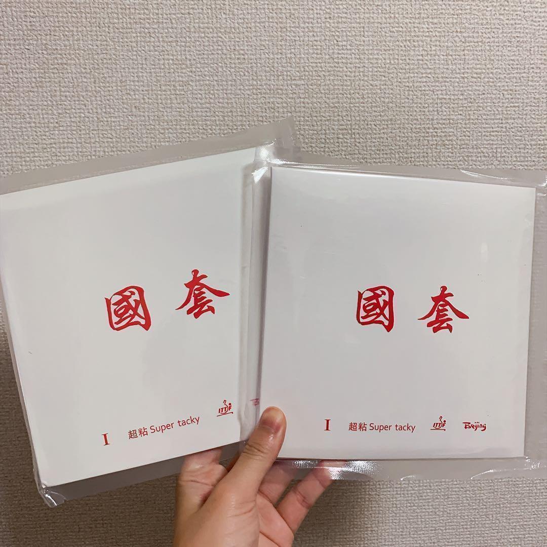 Two packaged table tennis racket rubbers in white sleeves with red Chinese characters held by a hand.