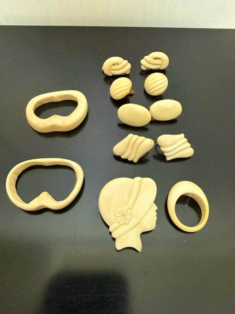 A set of pale carved accessories including a woman's profile brooch, rings, and multiple earrings arranged on a dark surface.