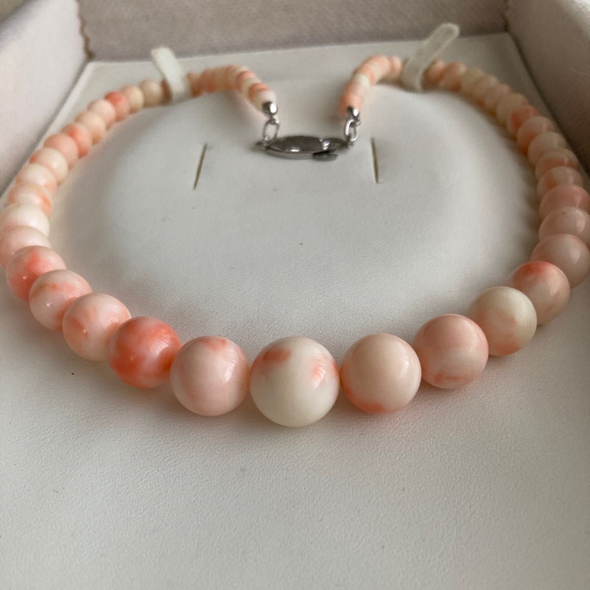 Pink gradient natural coral bead necklace with round beads and a silver clasp displayed in a jewelry box.