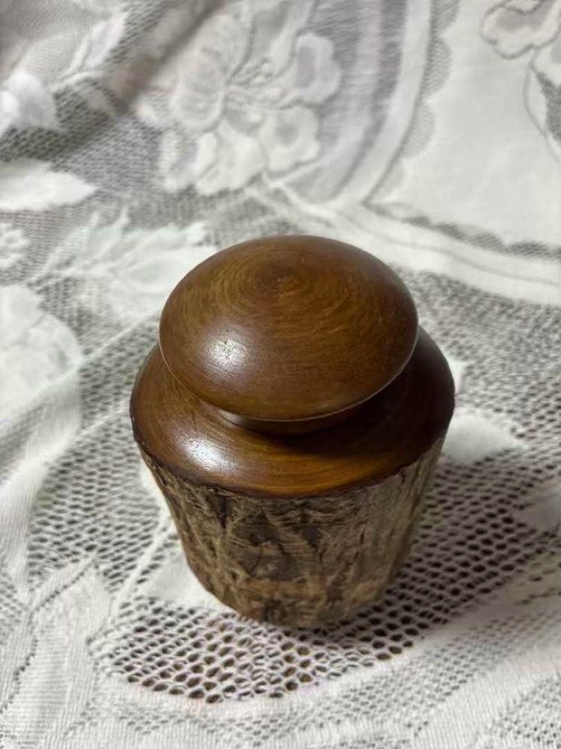 Wooden tea canister with natural bark exterior and a turned wooden lid shown on lace fabric.