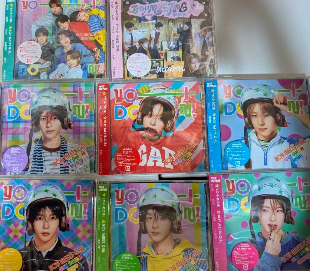 Photo of multiple NCT WISH YO-I-DON! BOY MEETS GIRL CD cases showing different member cover designs arranged in a grid.