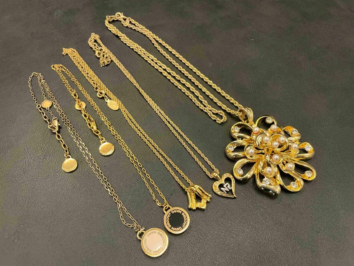 Five gold-tone non-precious metal necklaces with different pendants laid flat on a black surface.