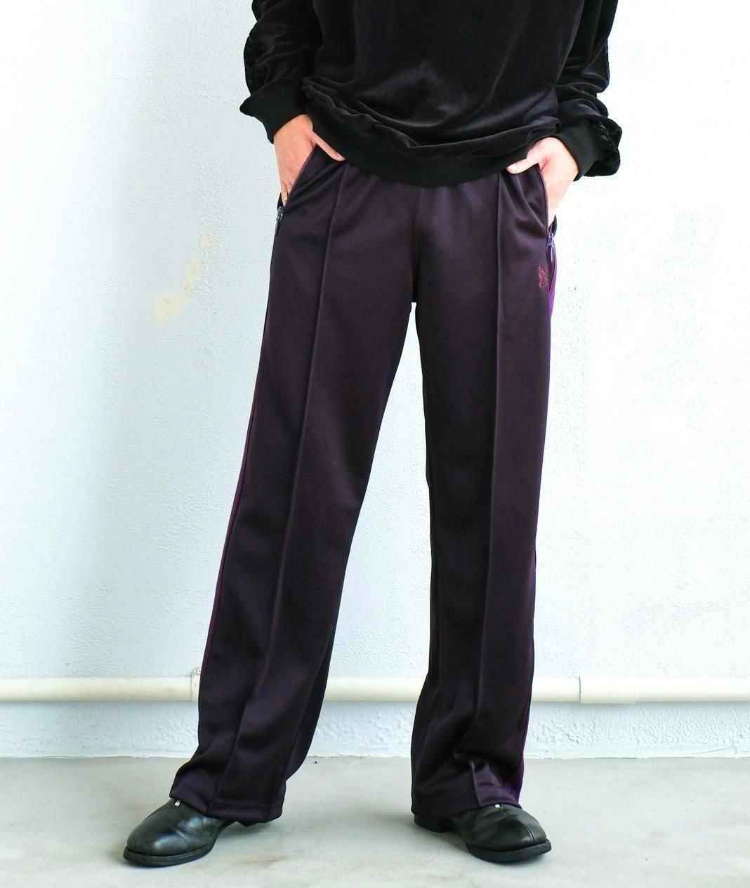 Front view of purple poly track pants worn by a model with hands in pockets.