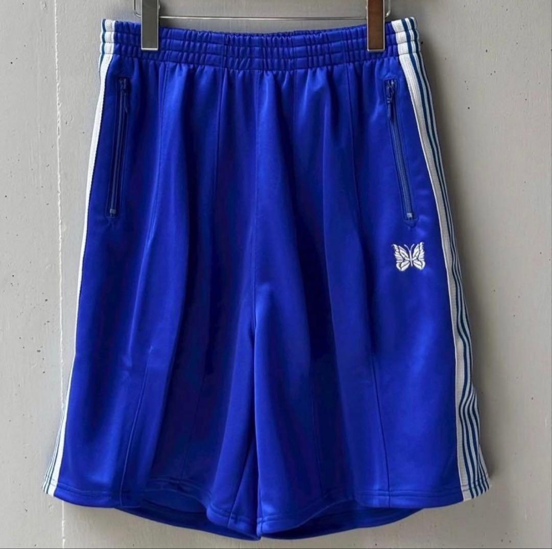 Blue Needles track shorts hanging on clips, front view showing white butterfly logo and white side stripes.