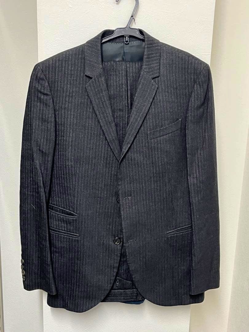 Front view of a dark gray NeIL BarreTT wool suit jacket hanging on a hanger.