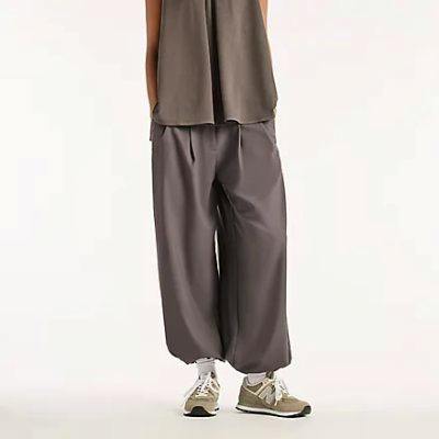 Model wearing NB grey loose-fit women's polyester easy pants shown from waist to shoes, paired with sneakers.