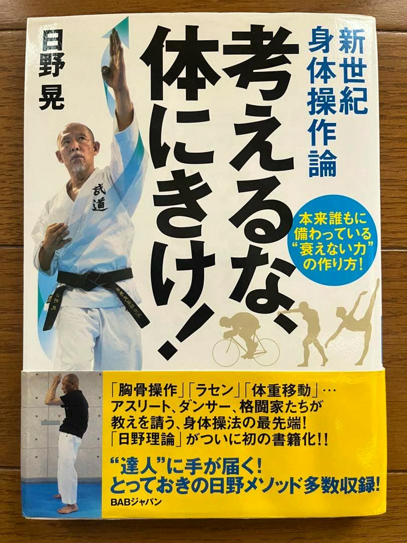Front cover of the book "新世紀身体操作論 考えるな、体にきけ！" showing large Japanese title text and a man in a white martial arts uniform raising his arm.