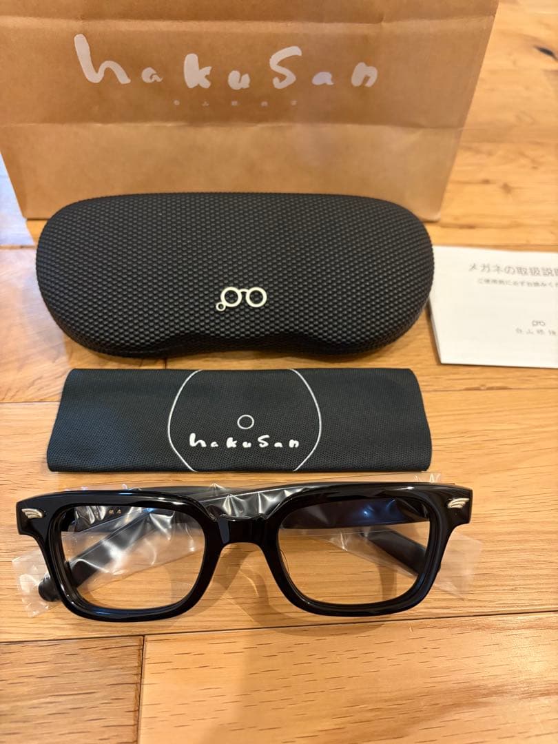 Front view of the glasses with corrective lenses displayed with a hard case, cleaning cloth, and packaging on a wooden surface.