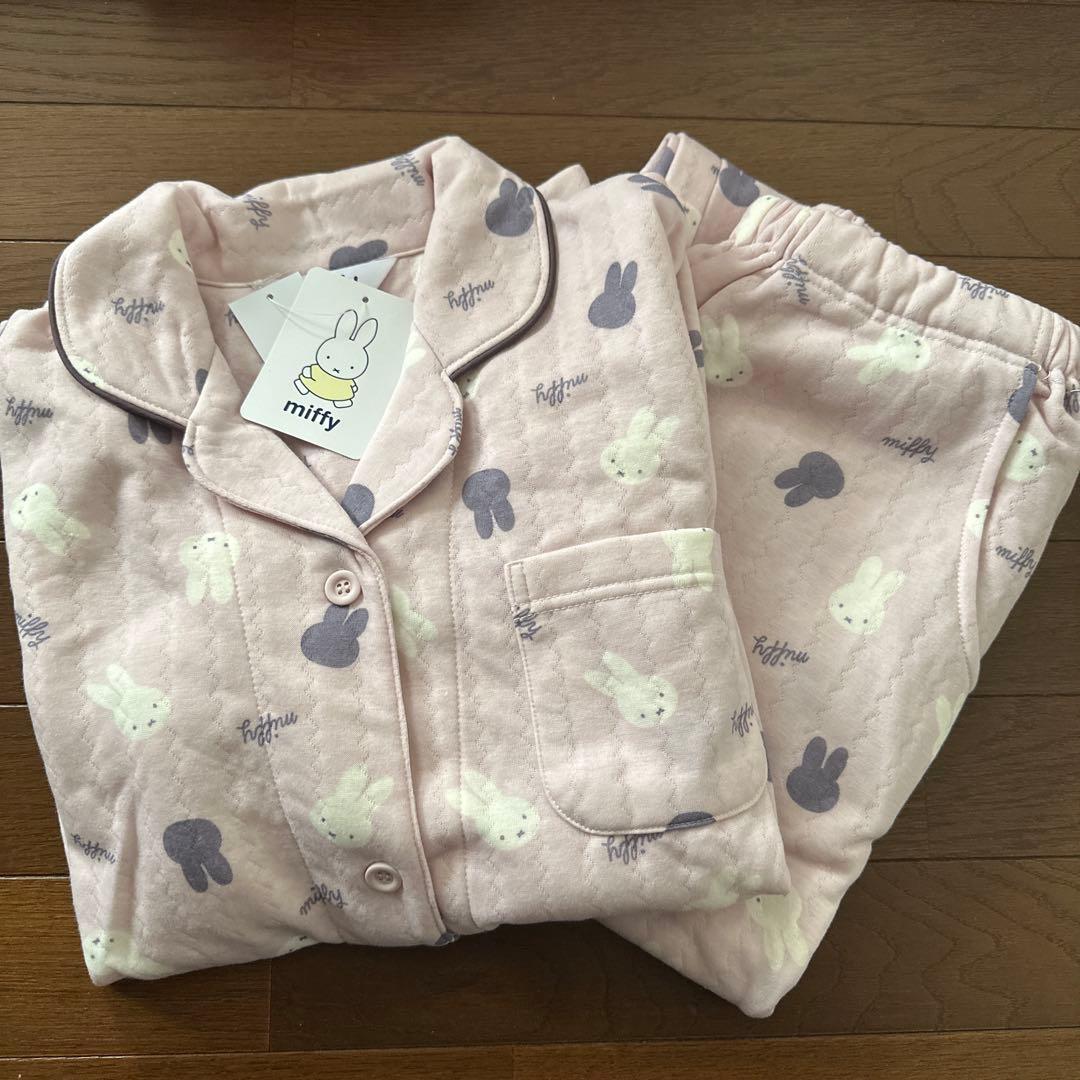 Folded pink Miffy women's pajama set with rabbit print and matching pants on a wooden floor.