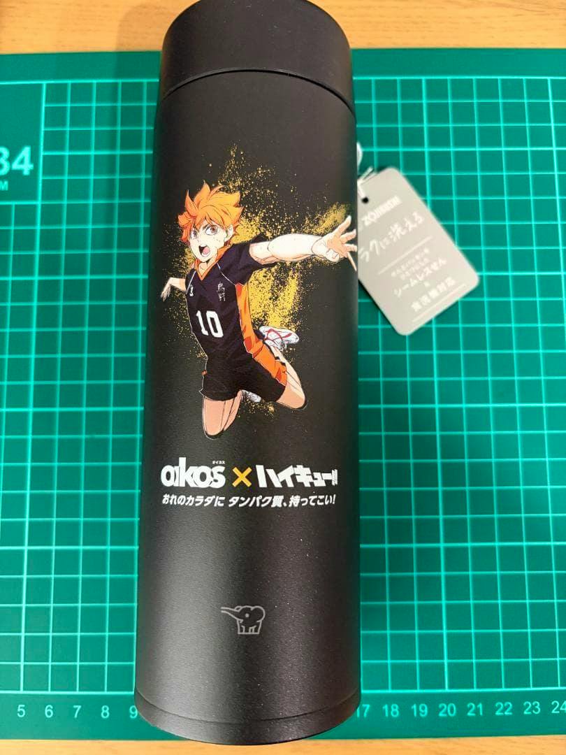 Black Zojirushi stainless mug featuring Oikos × Haikyuu anime artwork and a hanging tag, photographed on a green cutting mat.